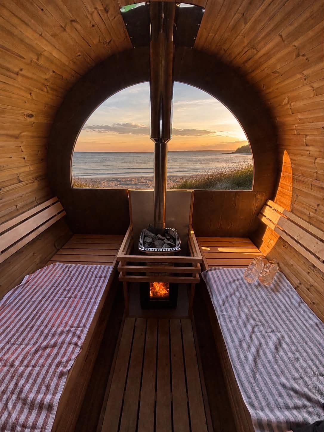 Indvendigt kig i SaunaSetup sauna med brændeovn og udsigt til solnedgang over havet