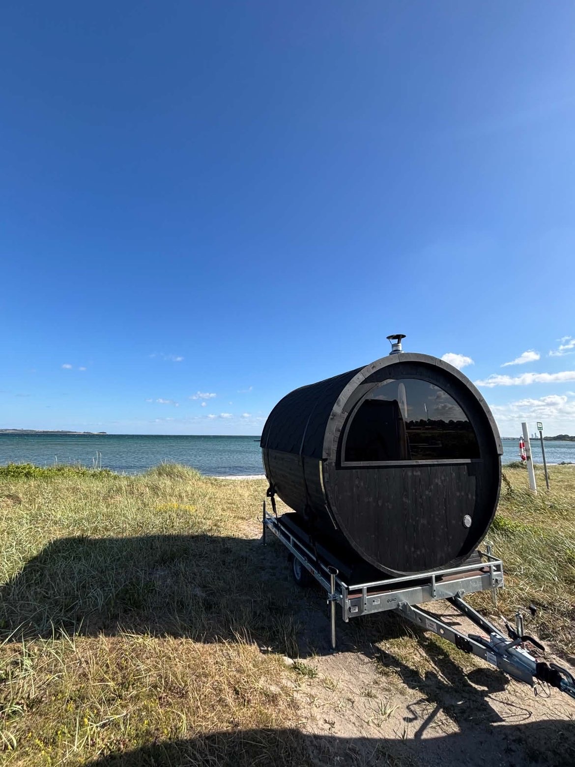 SaunaSetup mobil tønde-sauna på trailer ved stranden med havudsigt
